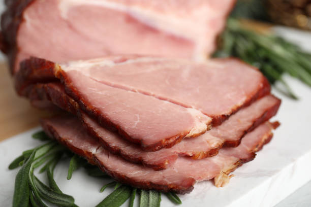 istock Cut delicious ham with rosemary on white table, closeup 1405991170