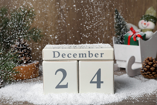 December 24 - Christmas Eve. Snow falling onto wooden block calendar and festive decor on table