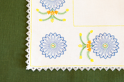 Detail of embroidery on a tablecloth in the form of blue cornflowers, on a green textural background. Sample of machine embroidery.