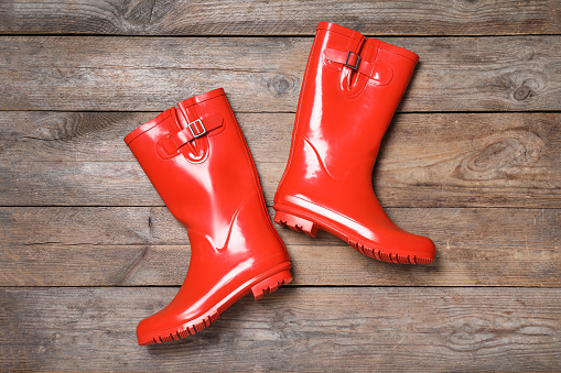 Pair of red rubber boots on wooden background, top view