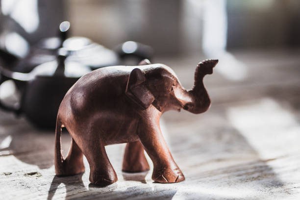 Decorative figurine of an elephant made of wood and teapots made of clay, on a wooden table Decorative figurine of an elephant made of wood and teapots made of clay, on a wooden table. Bright sunlight from the window, hard shadows elephant figurine stock pictures, royalty-free photos & images
