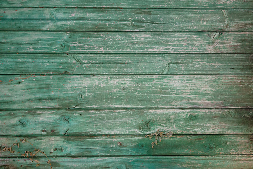 Grunge background texture of planks on a wooden wall with peeling green paint in a faded condition.