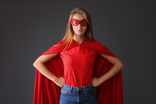 Confident woman wearing superhero cape and mask on grey background