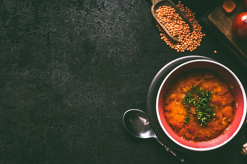 Red lentil soup with spoon in bowl on dark rustic background , top view with copy space. Vegan and vegetarian food