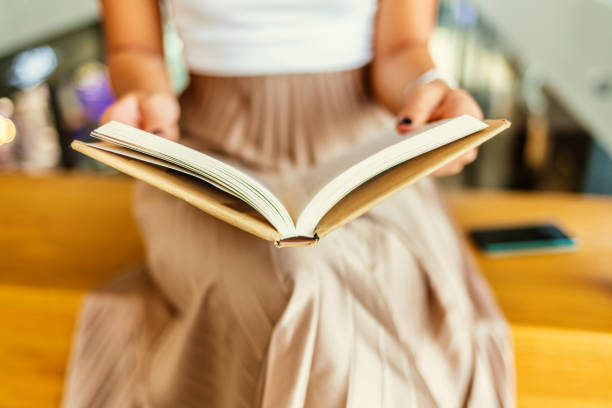 Shot of an unidentifiable young woman reading a book while enjoying a cup of coffee during the day.