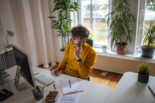 istock Caucasian man talking on mobile phone while working on computer in the office 1405996575