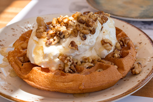 A large waffle covered with Greek yogurt, honey, and walnuts