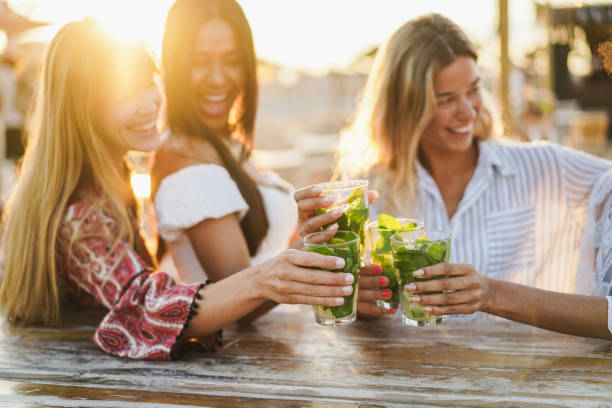 wielorasowe dziewczyny bawiące się przy koktajlach w barze na plaży - skup się na przednich rękach trzymających drinki - friendship relaxation cocktail nightclub zdjęcia i obrazy z banku zdjęć