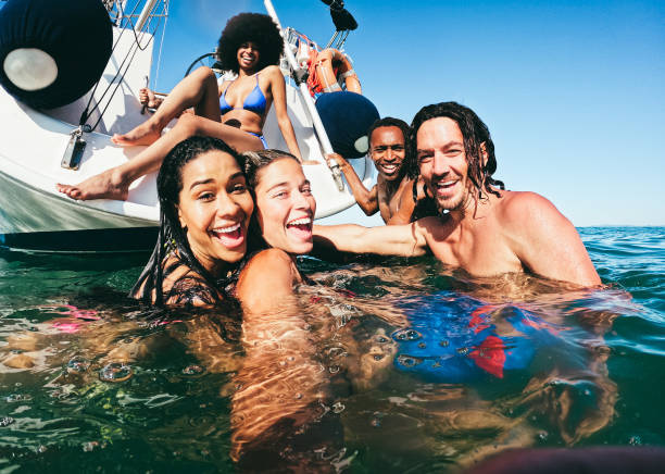 背景に帆船で海で自分撮りを泳いでいる幸せな多人種の友人 - 右の男の顔に焦点を当てる - friends on the beach ストックフォトと画像