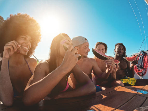 счастливые многорасовые друзья едят арбуз во время морского тура на парусной лодке - сосредоточьтесь на лице африканского мужчины - cruise ship cruise beach tropical climate стоковые фото и изображения