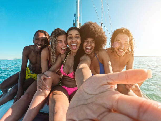 セーリングボートで海のツアーをしながらスイカを食べる幸せな多人種の友人 - センターガールの顔の主な焦点 - sunset yacht luxury sailboat ストックフォトと画像