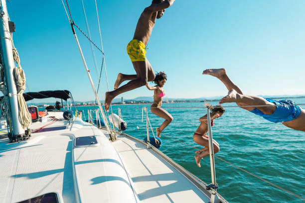Happy friends diving from sailing boat into the sea - Focus on left girl face right man face Happy friends diving from sailing boat into the sea - Focus on left girl face right man face ibiza island stock pictures, royalty-free photos & images