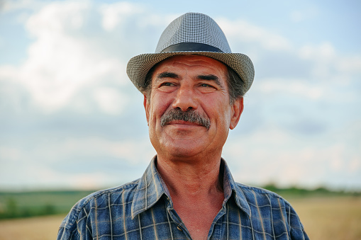 close up of a human head aged farmer with mustache against in the sky background. old male farmer worker with arms crossed. front view.