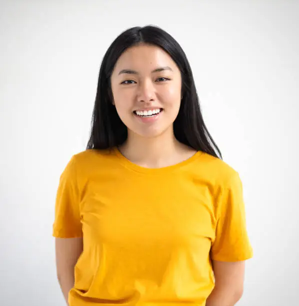 Photo of Portrait of cheerful Asian woman with happy smile. Young female student smiling joyfully standing on a white background