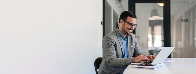 Cheerful male business professional in formals working on laptop while sitting at office desk