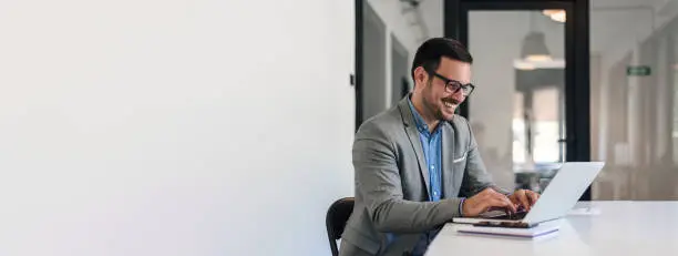 Photo of Cheerful business professional working on laptop while sitting at office desk