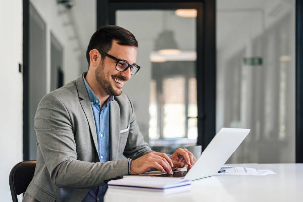 istock Smiling young businessman typing on laptop while working at office desk 1406002843