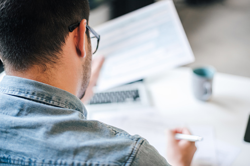 Rear view of male freelancer working over documents while sitting at table in home office