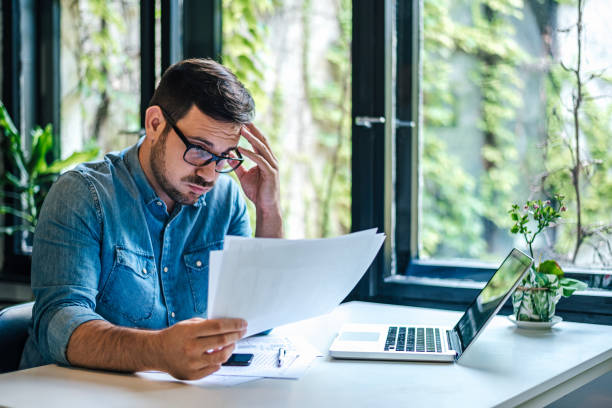 istock Stressed businessman reading documents while working on laptop at home office 1406002880