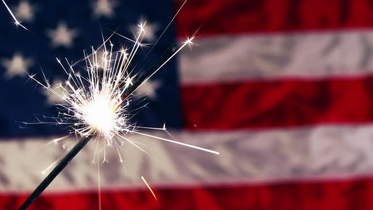 a sparkler firework with a USA Flag in the background.