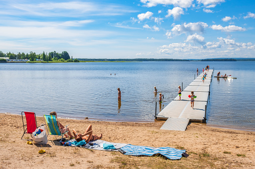 Karlsborg, Sweden - July 17, 2019: Beach at a lake with people that are sunbathing and bathing children
