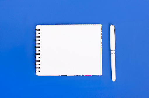 Top view of blank spiral notepad with pen isolated on blue background for mockup. Minimal design, copy space