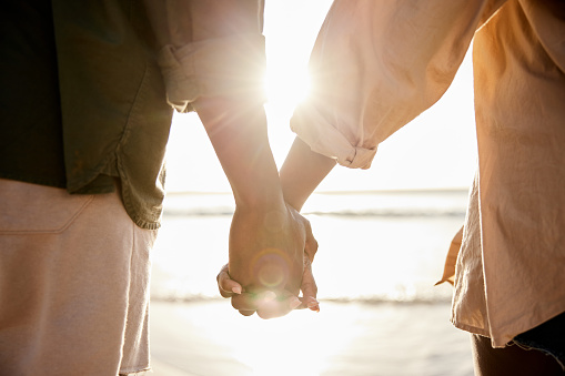 Close-up of a loving young African couple standing hand in hand together on a sandy beach and watching the sunset over the ocean