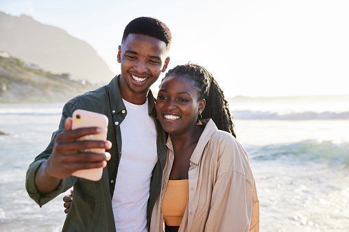 Smiling young couple taking a selfie while enjoying a day at the beach together on a sunny afternoon in the summertime