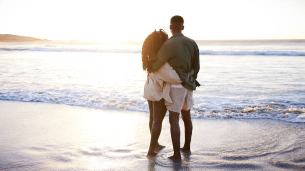 istock Young couple standing arm in arm on a beach and watching the sunset 1406013340