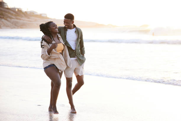 istock Laughing young couple walking arm in arm along a sandy beach 1406013403