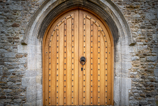Newly renovated medieval wooden door seen at the entrance to a very of medieval English church. The ornate archway is seen together with the renovated stonework.