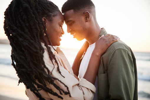 Couple standing arm in arm with their eyes closed on a beach at sunset