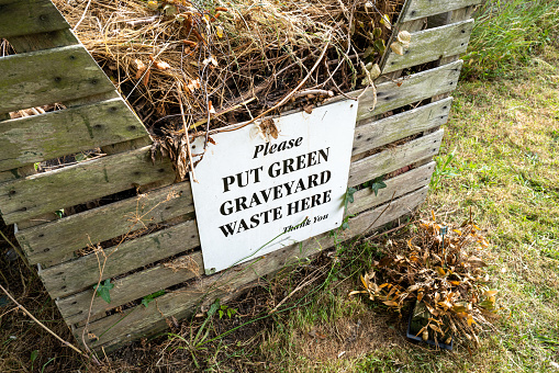 Generic green waste sign seen on a wooden collection crate used for visitors to discard dead flowers in a rural cemetery.