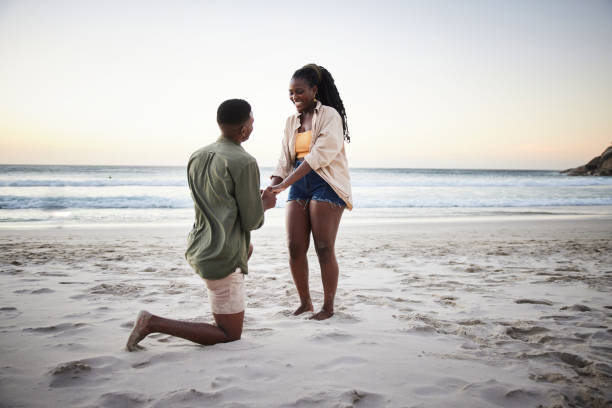 jovem pedindo a namorada em casamento em uma praia de areia ao anoitecer - noivado - fotografias e filmes do acervo