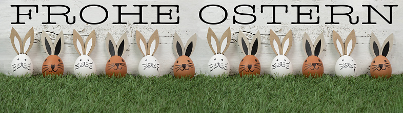 Happy Easter background greeting card - Many brown and white Easter eggs with bunny ears / Easter bunnies on fresh green meadow, isolated on white vintage shabby wall texture