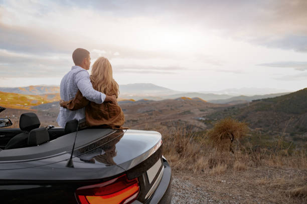 istock Cute caring man hugging his girlfriend standing or roadside looking at mountains. Rear view 1406018757
