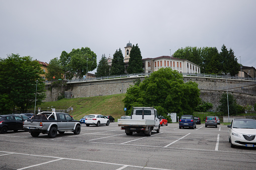 Borgo Val di Taro, Italy - June, 2022: Free parking in small Italian town near old town wall and view to bell tower of Parrocchia Sant Antonino church. Half-empty outdoor parking lot in Borgotaro