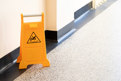 Caution wet floor orange fold out sign without text in a bright corridor, closeup detail Slipping man symbol, object up close, nobody, copy space Accidents, at work, cleaning services abstract concept