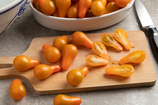 Cutting board with yellow whole and halved pear tomatoes close up in the kitchen