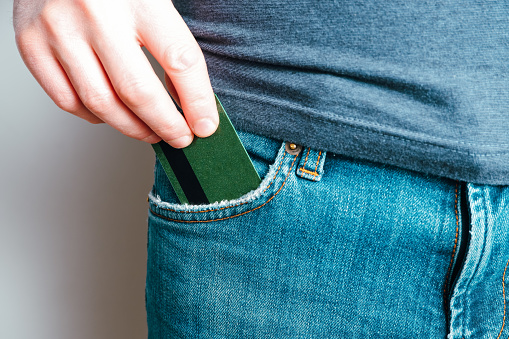 A young man takes out a credit card from his blue jeans pocket. Close-up on a hand taking out a payment card from trousers on a light background.
