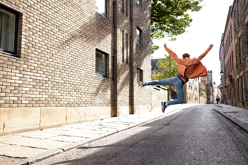 A young man spending the day in Durham, England. He is jumping in the air with his arms in the air as well.