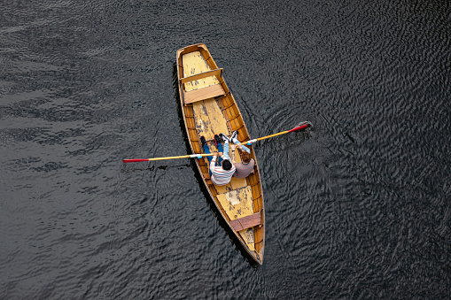 Directly above of a male couple spending the day in Durham, England together. They are sitting in a rowboat and using one oar each to row the boat along the river.