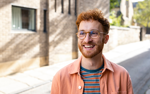 A young man spending the day in Durham, England and exploring the city. He is standing on a city street while looking to his side and smiling.