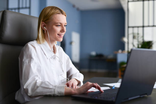 Woman sits in front of her laptop looking at screen and smiling stock photo