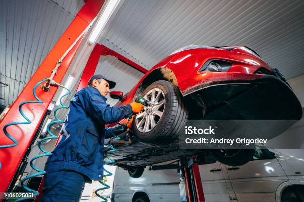 Expert Specialist Technician Changes Tires Tyres Of Lifted Up Car At Auto Service Wears Uniform Costume Stock Photo - Download Image Now
