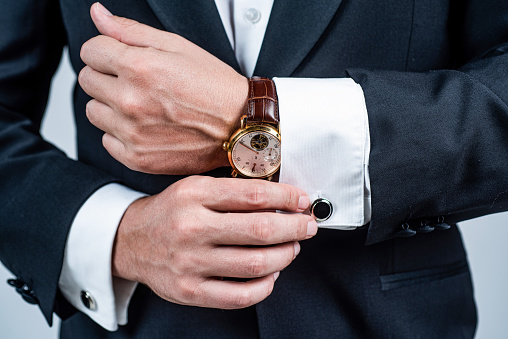 Modern horology. Wrist watch worn with formal suit. Portable timepiece. Time management. Horology concept. Professional punctuality. Business etiquette.