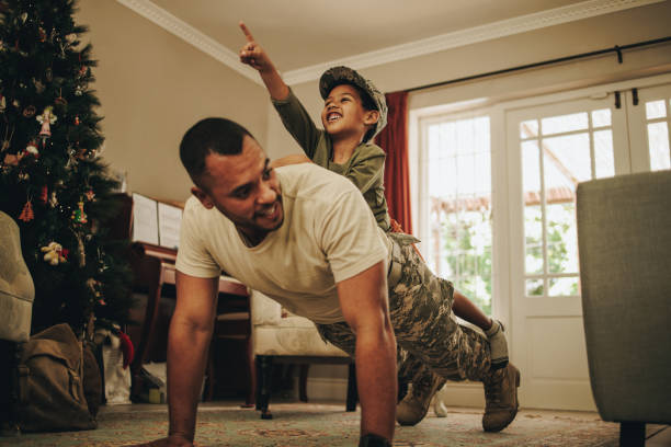 Military dad bonding with his son at Christmas Military dad bonding with his son at Christmas. Happy army soldier spending the holidays with his child after deployment. Father and son having a playful reunion at home. military lifestyle stock pictures, royalty-free photos & images