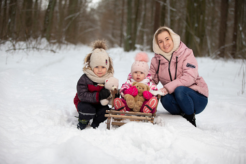 Mom and children on a vintage wooden sled against the backdrop of a winter forest. Woman with children on a winter walk.