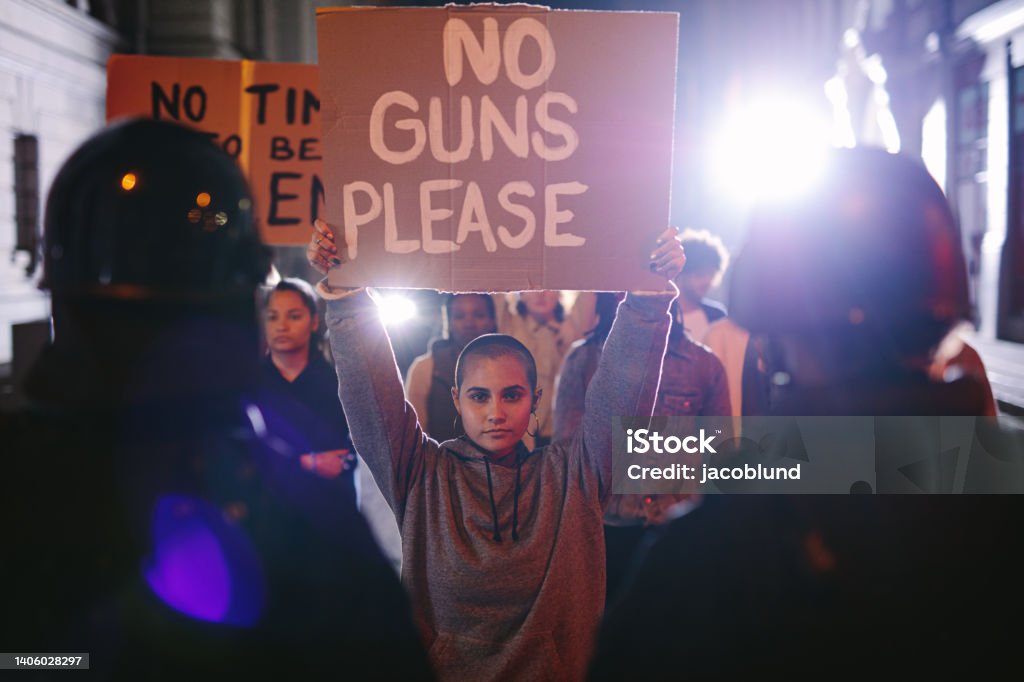Activists protesting for gun control Group of protestors with banners for gun control in front of police force. Activists demonstrating to ban weapons at night. Gun Violence Stock Photo