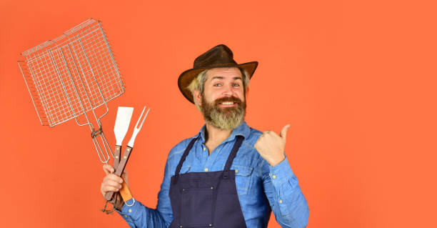 istock summer weekend. happy hipster hold cooking utensils for barbecue. bearded man chef. Tools for roasting meat outdoors. Picnic and barbecue. ready for barbecue party. Culinary concept. copy space 1406033312